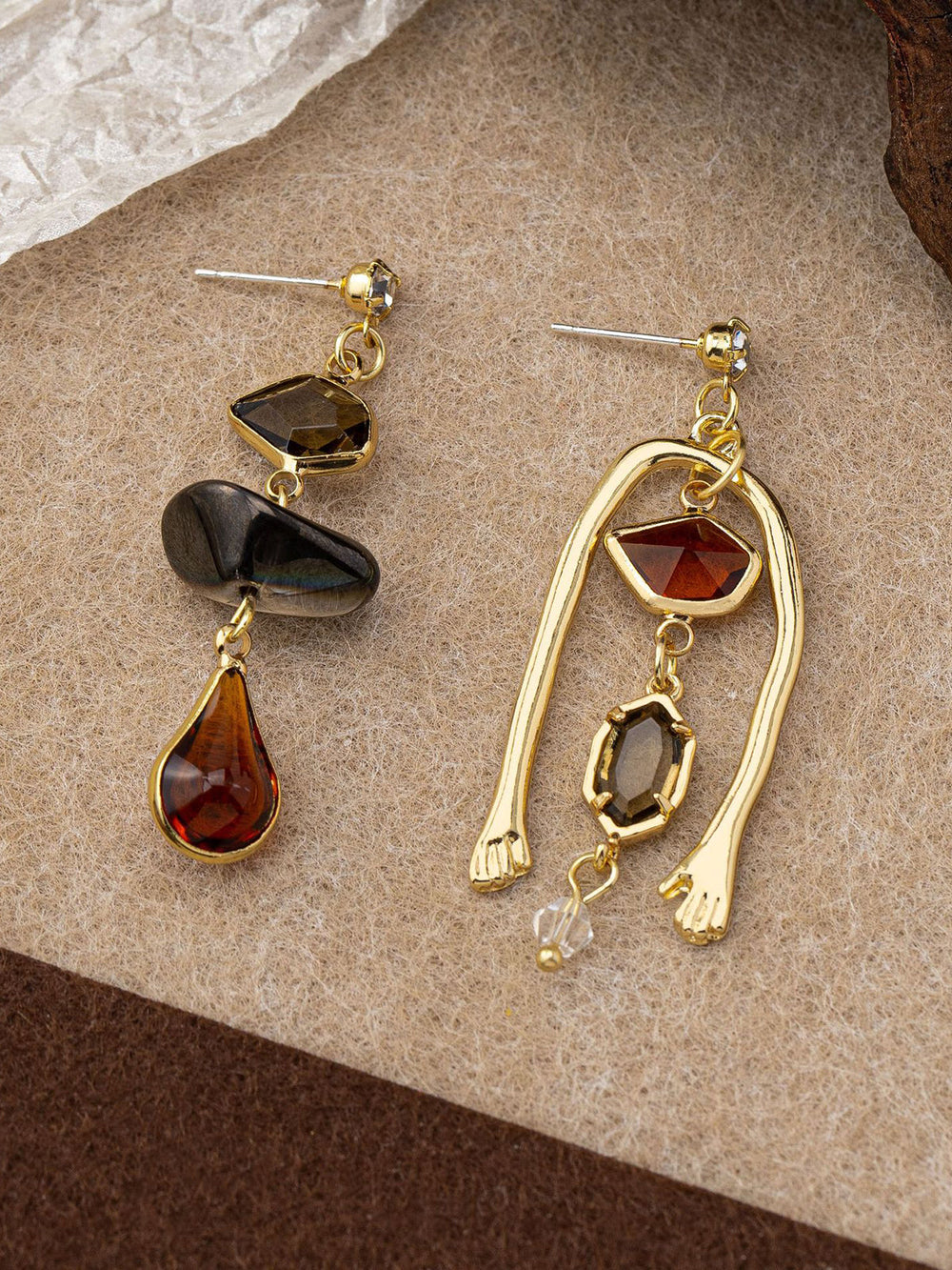 Boucles d'oreilles pendantes asymétriques en pierres précieuses avec détail de main